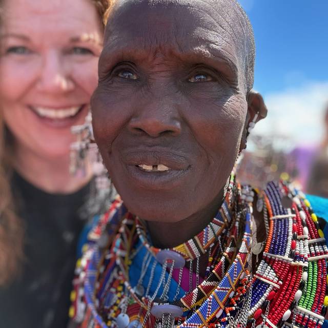 A Maasai elder in beadwork smiling beside a visiting team member