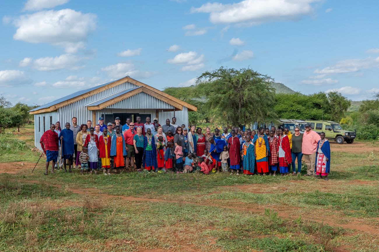 A newly built church of corrugated iron with a blue roof, its congregation and a visiting team gathered in front of it