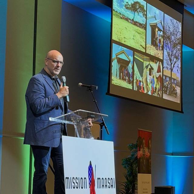 A speaker at the podium at the Annual Banquet, photographs from Kenya on the screen