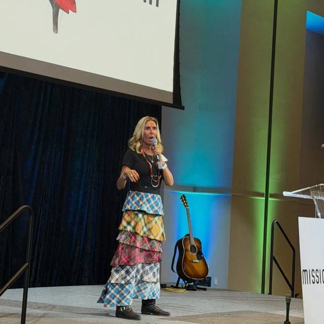 A speaker on stage at the Annual Banquet, the Mission Maasai logo on the screen behind her