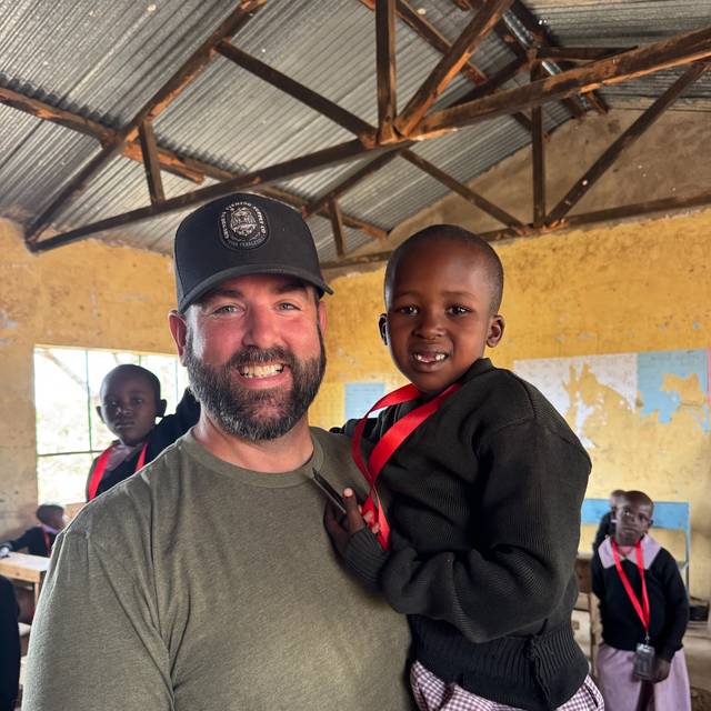 A visiting team member holding a young student in a classroom, both smiling