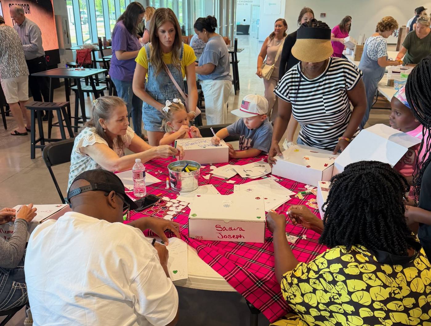 Families around a table at Christmas in July, decorating gift boxes and writing notes of encouragement to send with them