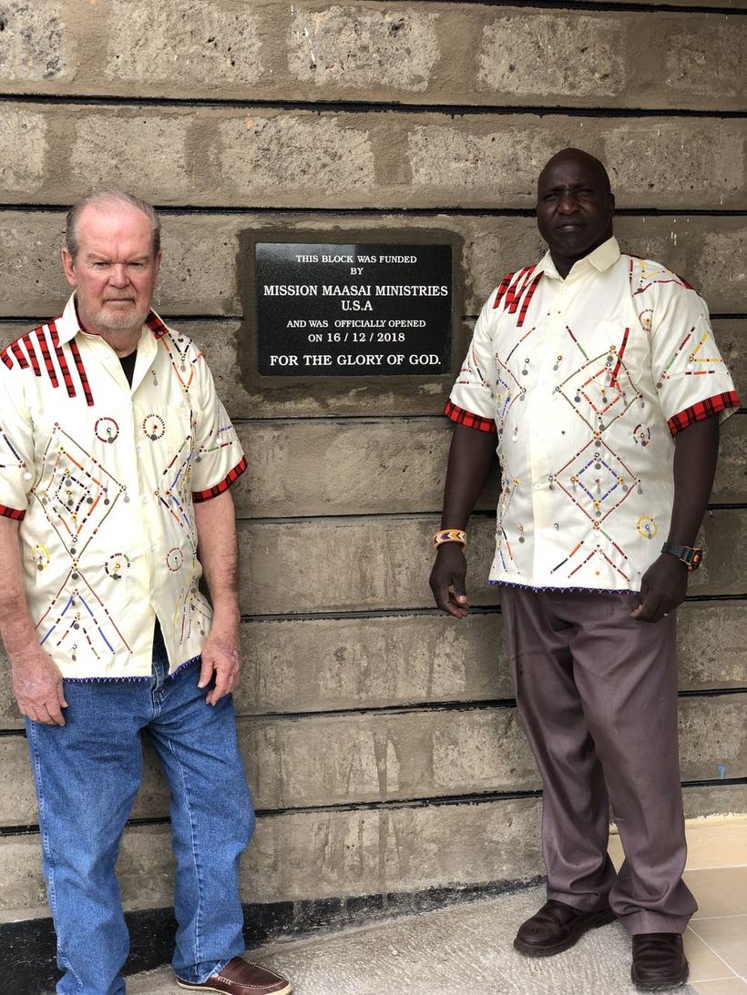 Mike Nevil and Pastor Timothy Moilo standing either side of a dedication plaque reading: This block was funded by Mission Maasai Ministries U.S.A and was officially opened on 16/12/2018, for the glory of God