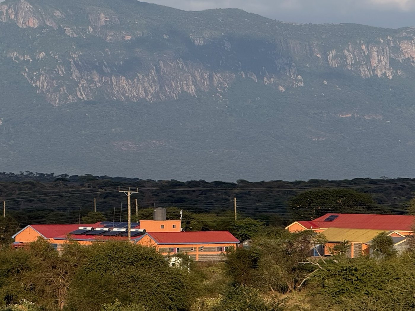 Power lines on wooden poles running past the Empukani Medical Clinic, a mountain ridge behind