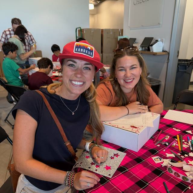 Two volunteers decorating gift boxes and writing notes at the craft table