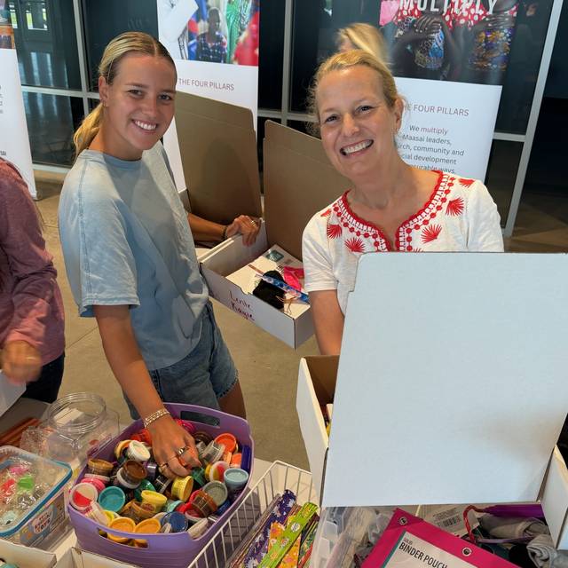 Two volunteers filling boxes from bins of small toys and supplies