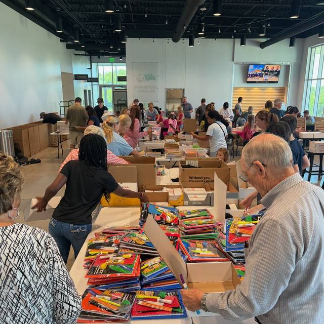 Volunteers working down a long table of school supplies, filling boxes for Empukani